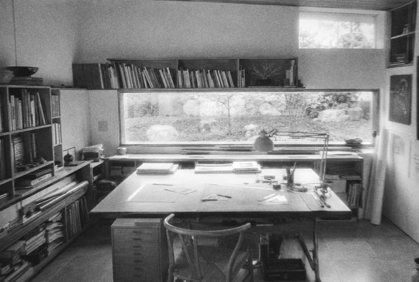 A drawing board at a window, shelves of books above it