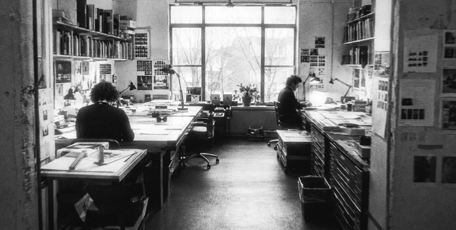 A shared studio, two people at their desks by the window